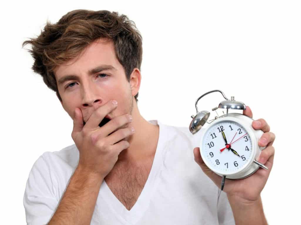 Yawning man holding alarm clock