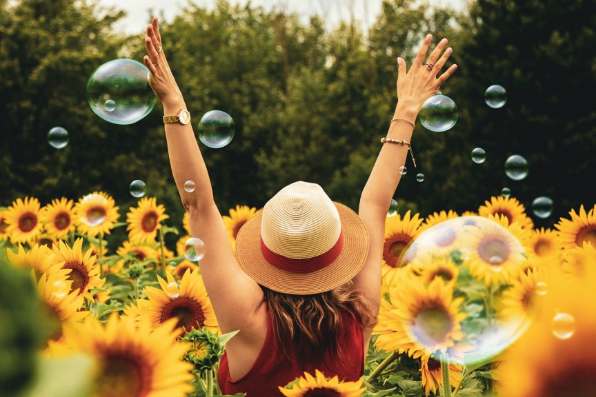 Frau steht in einem Sonnenblumenfeld und hat die Hände in der Luft.